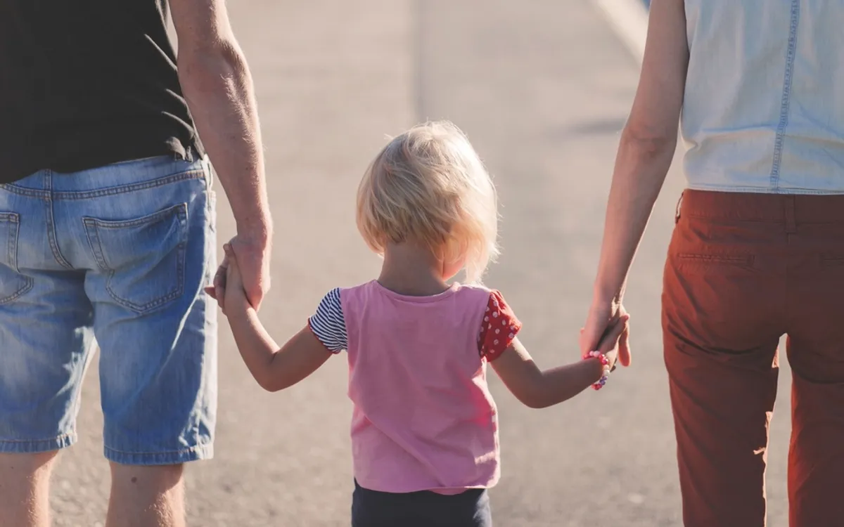 A mother, father and child walking hand in hand, seen from behind