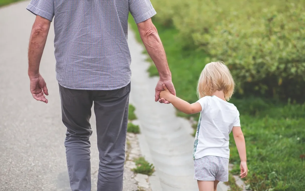 A father and a small child walking hand in hand, seen from behind
