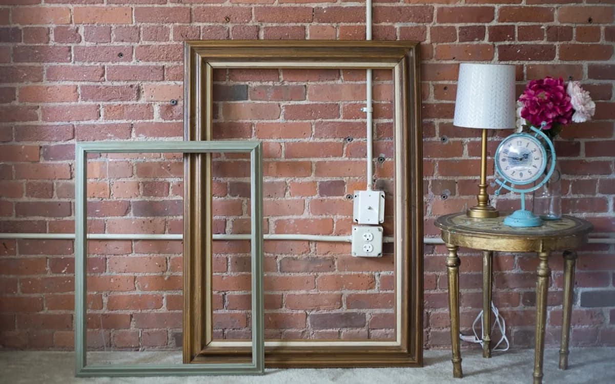 Vintage picture frames, an old clock and flowers against a brick wall