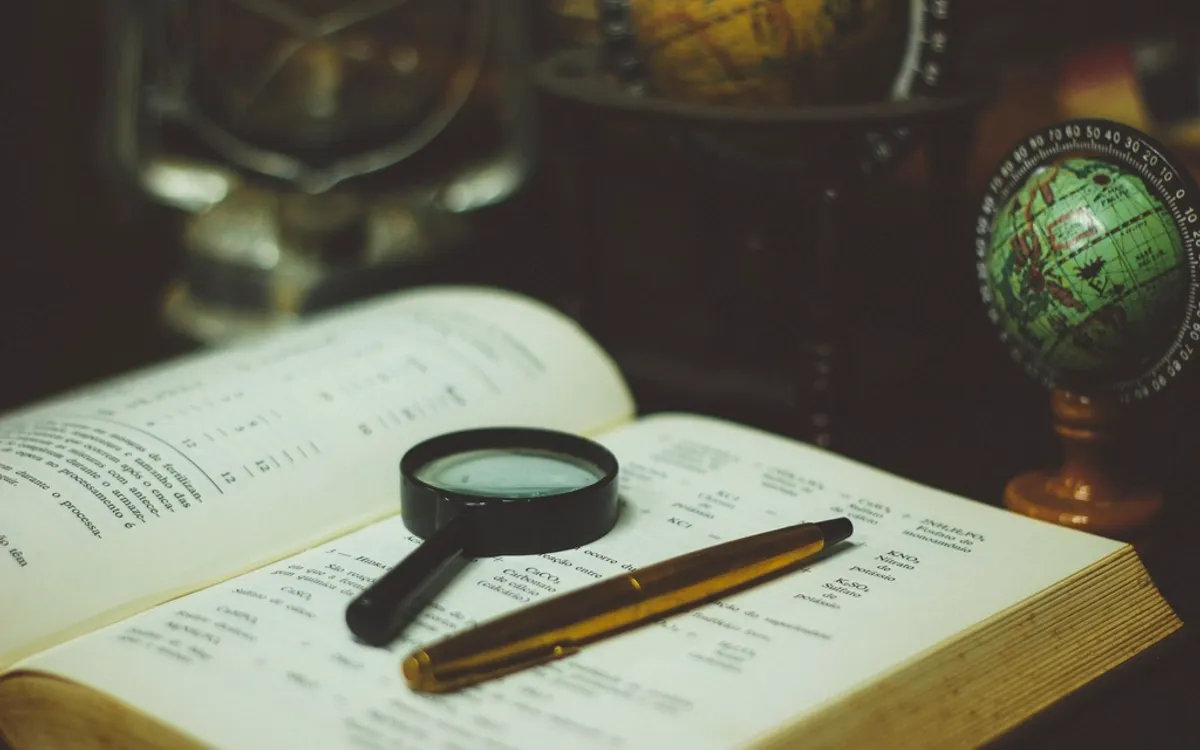 A magnifying glass and fountain pen on an open book, a globe behind
